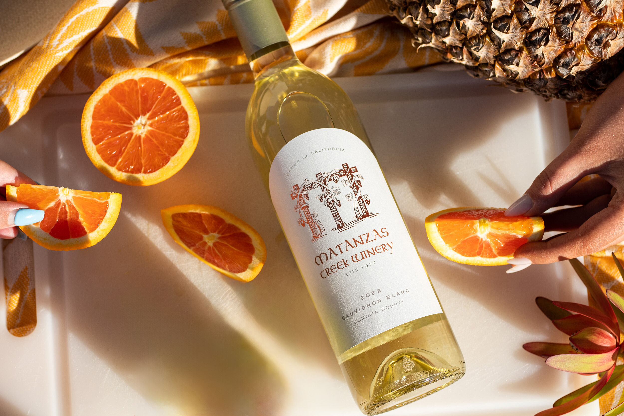 A bottle of white wine on a white cutting board with slices of orange around it, and a yellow blanket.