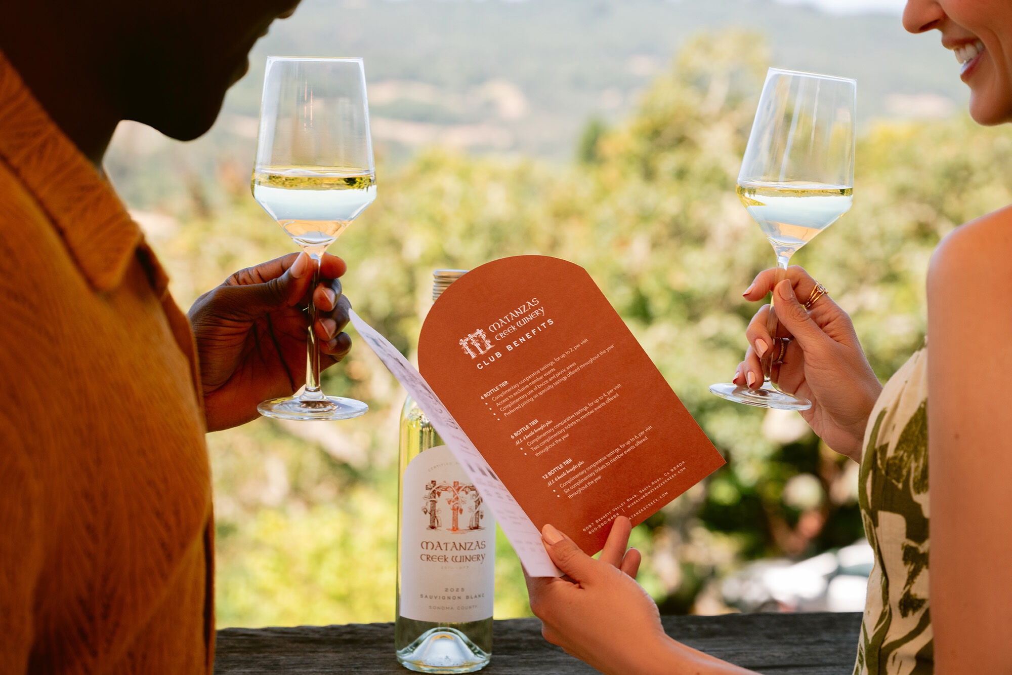 A close up on two people looking at a pamphlet with glasses of wine wine in-hand.